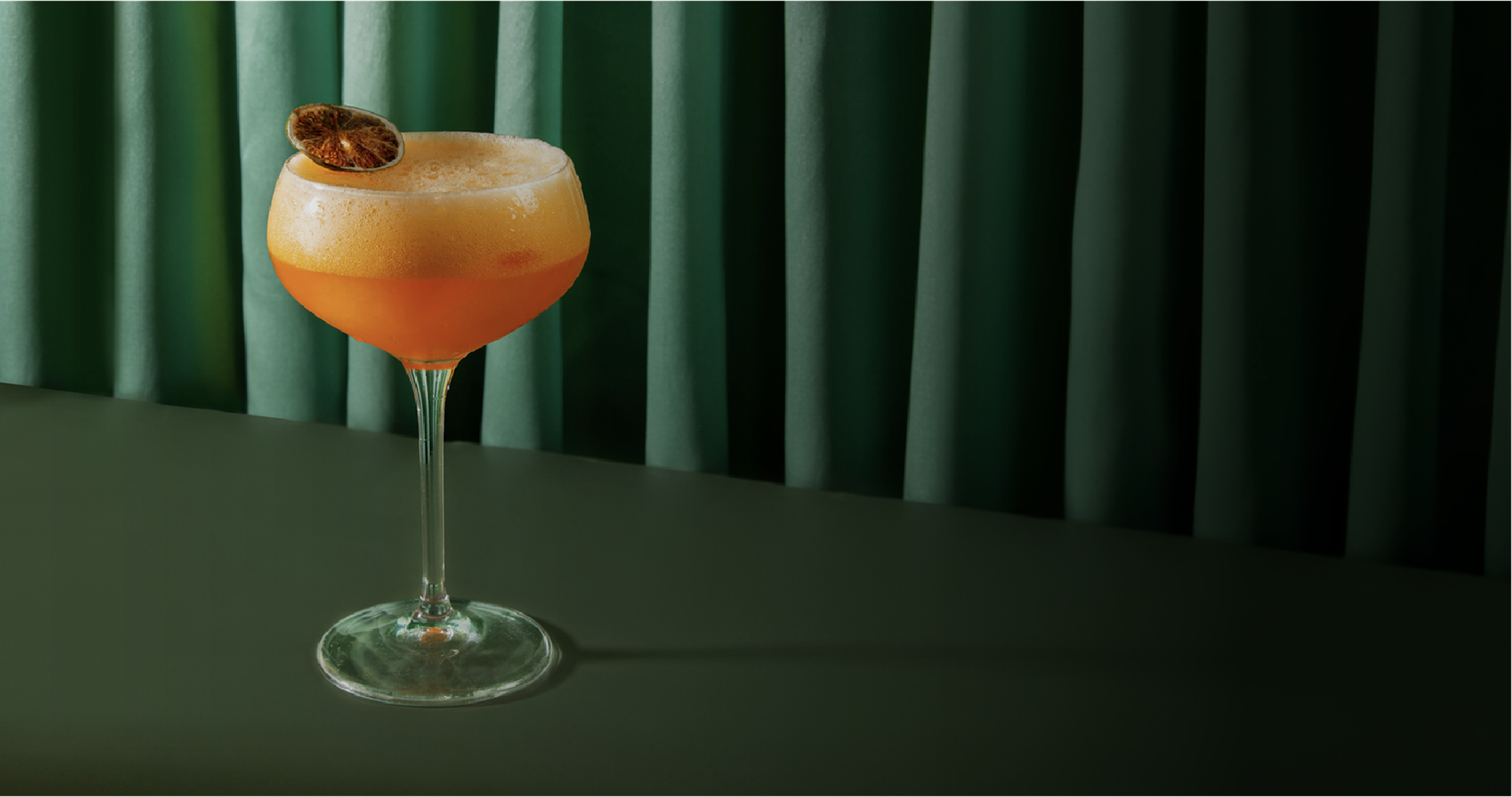 A beautiful orange coloured cocktail on a green table.